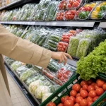 Main de cliente hésitant entre fruits emballés et fruits en vrac au supermarché